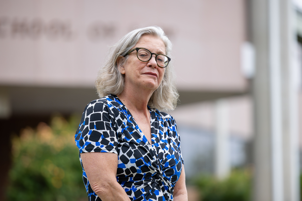 Mid shot of Professor Hassel wearing eye glasses and a blue and black patterned dress