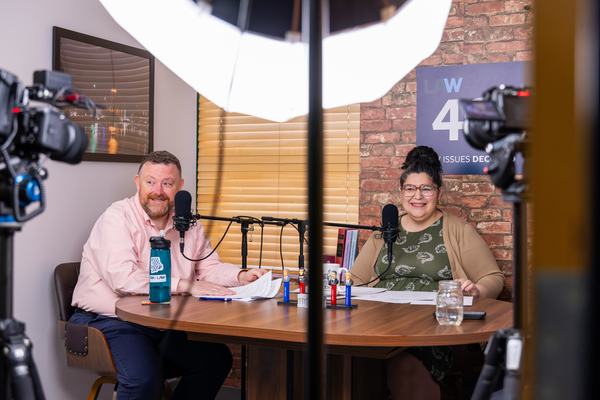 Two podcast hosts recording together at a studio table.