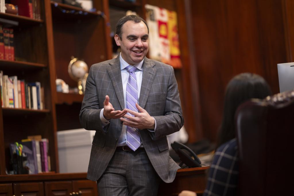 Man leaning against office desk with bookcase behind him