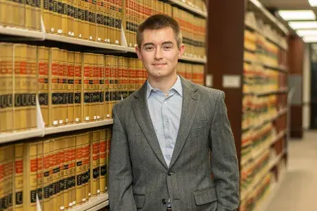 Male law student wearing gray suit jacket with bookshelves behind him