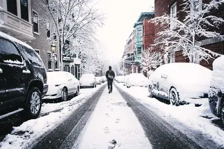 Man walking down middle of snow covered city street