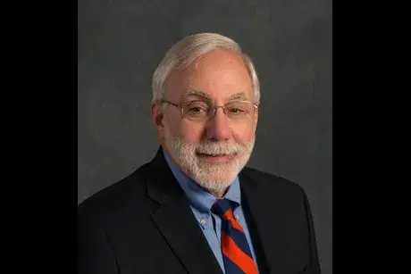 Close up shot of Professor Kogan with gray hair and beard, wearing a suit.