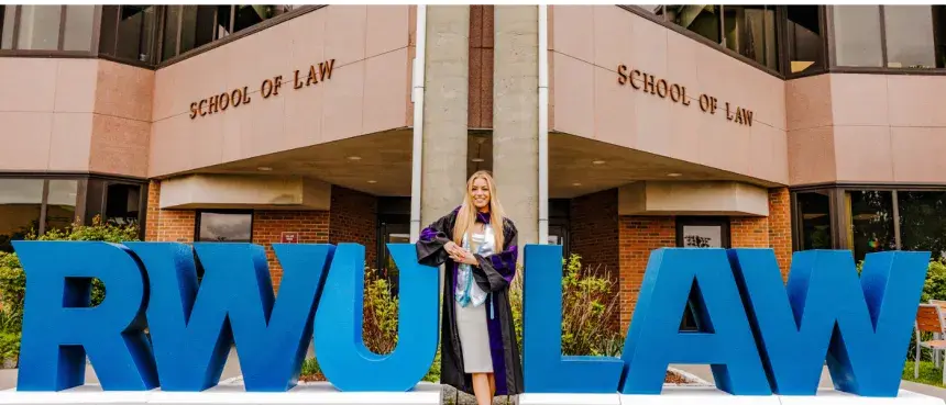 Graduating student in front of building flanked by larged RWU and LAW letters on each side.